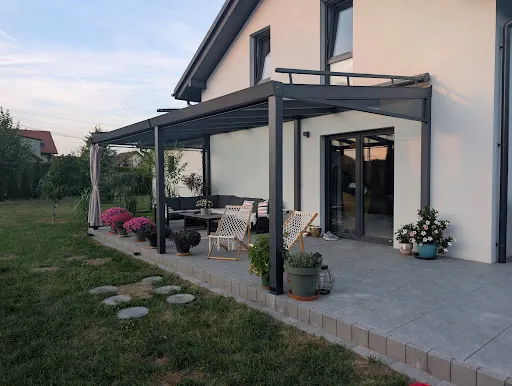 Zadaszony taras w Jankowicach z markizą nad szklanym dachem, meblami ogrodowymi i kwiatami
