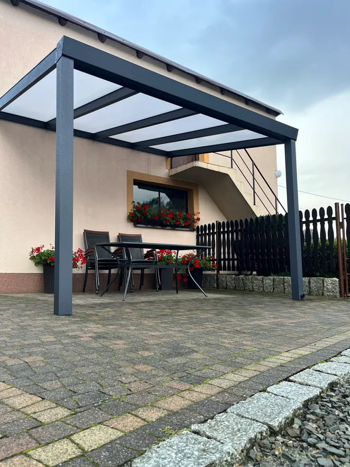 Grafitowe zadaszenie z jasnym dachem nad stołem i krzesłami w Jarząbkowicach