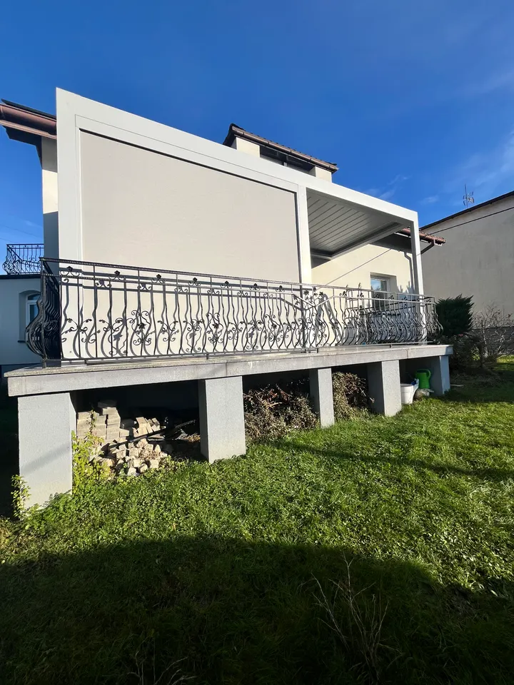 Jasna pergola lamelowa z opuszczoną osłoną na podwyższonym tarasie w Gorzycach