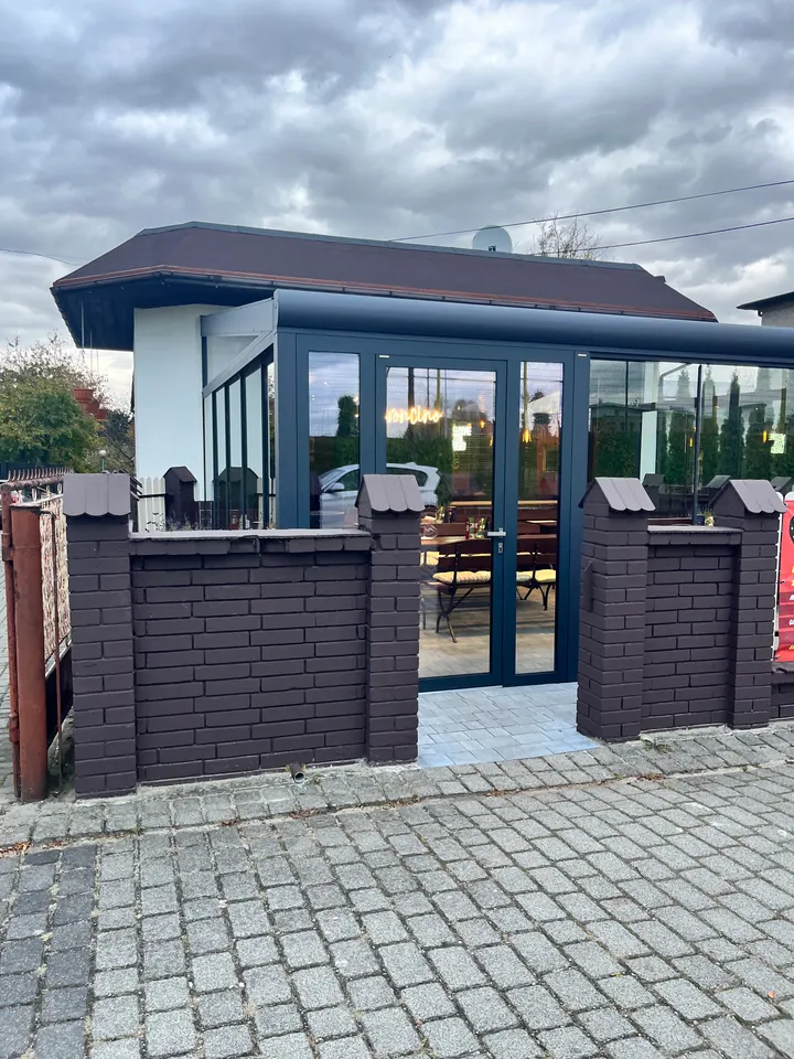 Szklane drzwi wejściowe w zabudowie ogródka restauracji w Pawłowicach, widok z zewnątrz