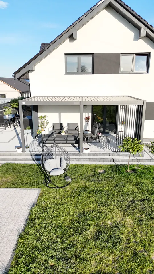 Grafitowa pergola w Żorach z pionowymi panelami i meblami ogrodowymi, widok od strony trawnika