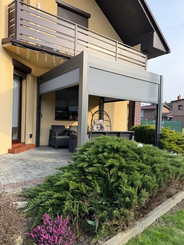 Pergola z częściowo opuszczonymi szarymi roletami przy domu w Żorach