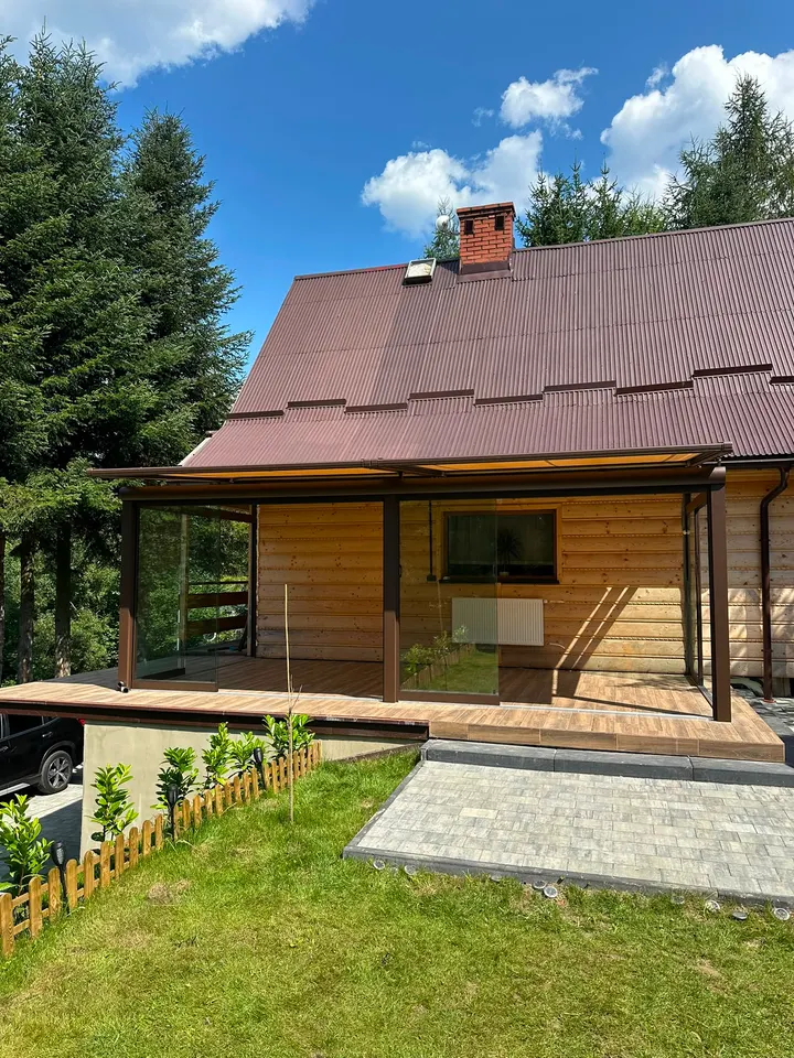 Brązowa szklana zabudowa tarasu przy drewnianym domu w Suchej Beskidzkiej, widok od frontu